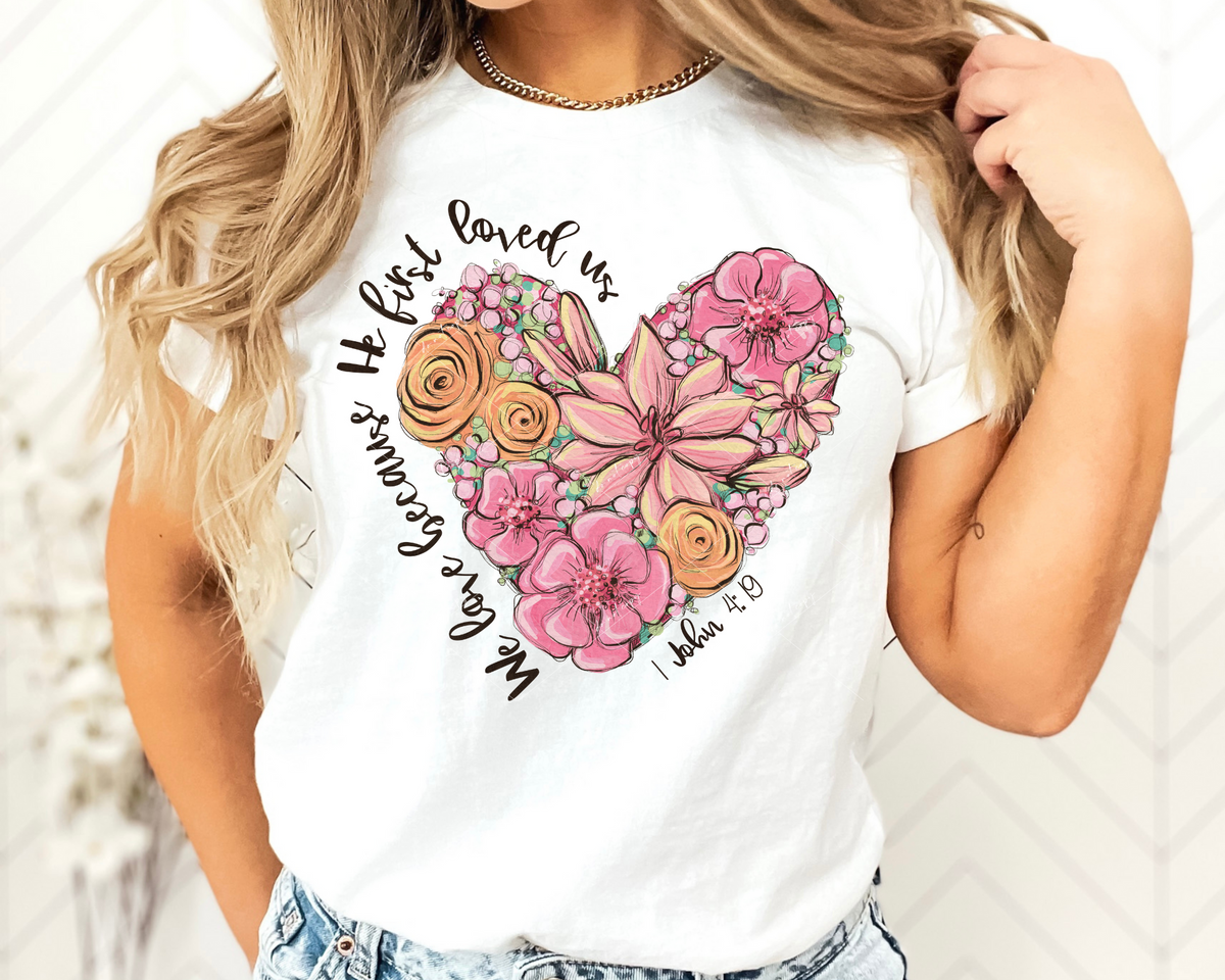 We love because He first loved us. 1 John 4:19 (heart shape of large flowers, pinks, coral, yellow colors, black lettering) 1900 DTF TRANSFER